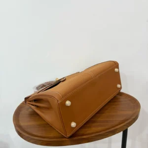 Hermes Kelly Lakis 28 handbag in gold and brown, showcasing the bottom view with decorative studs, on a wooden table, emphasizing luxury craftsmanship and design.