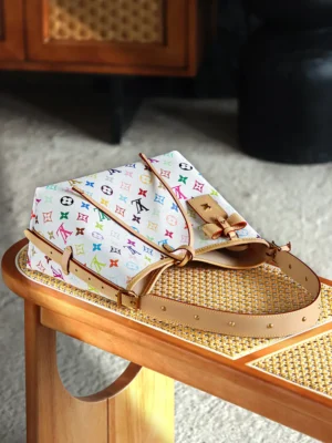 Carryall White Tri Color bag by Louis Vuitton featuring Murakami Takashi's design, displayed on a wooden table with a woven surface, showcasing vibrant multicolored logos and a brown leather strap.