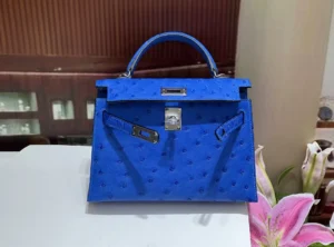 Herm&egrave;s Kelly bag 28 blue ostrich leather silver hardware handbag on white table with flowers