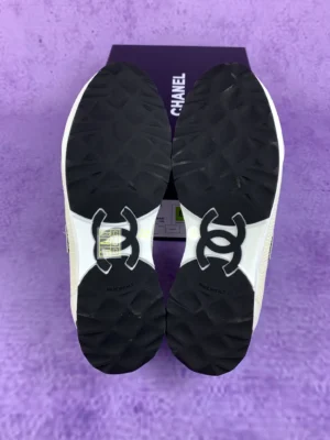 Chanel 25P series casual sports shoes, pure white, showing the outsole with iconic logo and detailed tread design, on a purple background.