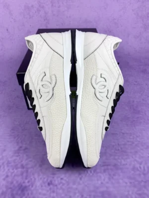 Chanel 25P series casual sports shoes in pure white, featuring iconic logo and black accents, displayed against a purple background.
