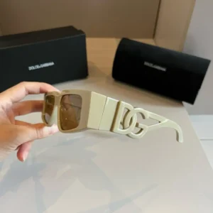Dolce&Gabbana's Sunscreen Sunglasses held in hand, featuring stylish design and logo, with packaging in background.