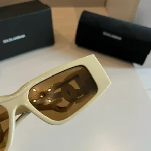 Dolce&Gabbana sunglasses with brown lenses and stylish frame, displayed with branded cases in the background, showcasing luxury fashion accessory.