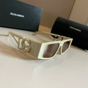 Dolce&Gabbana sunscreen sunglasses featuring a distinctive logo, displayed on a surface with branded packaging in the background.