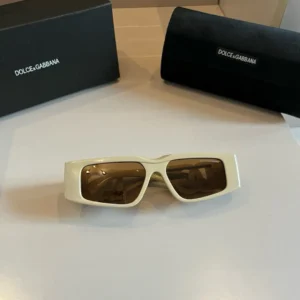 Dolce&Gabbana’s Sunscreen Sunglasses displayed on a table with branded packaging, showcasing stylish design and brown lenses.