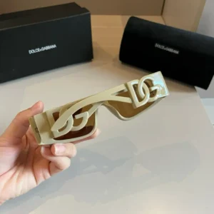 Dolce&Gabbana's Sunscreen Sunglasses held in hand, featuring a unique design and logo, with black boxes in the background.