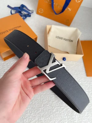 Hand holding a Louis Vuitton men's palm print belt with a stainless steel buckle, displayed against branded packaging, emphasizing quality replica luxury accessories.