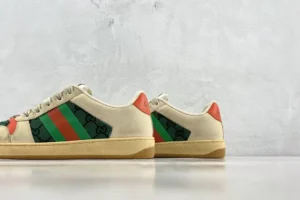 Gucci Screener Distressed Leather sneakers featuring green and red stripes, logo detailing, and a beige canvas upper, displayed on a neutral background.