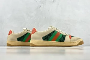 Gucci Screener Distressed Leather sneakers featuring a beige canvas upper with green and red stripes and a gum sole, displayed on a neutral background.