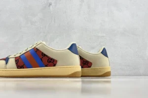 Gucci Screener Distressed Leather sneakers featuring a cream base with red and blue stripes and signature logo detailing, displayed against a minimalist background.