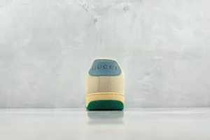 Gucci Screener Distressed Leather sneaker rear view, featuring a cream upper, green sole, and embossed logo on the heel, showcased against a minimalist gray background.