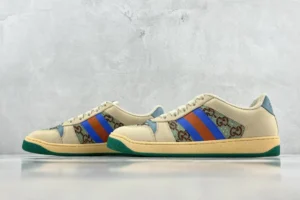 Gucci Screener Distressed Leather sneakers featuring beige upper with blue and orange stripes, iconic GG logo pattern, and green sole, available for purchase on e-commerce site.