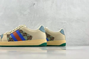 Gucci Screener Distressed Leather sneakers featuring a beige upper, colorful stripes, and signature logo detailing, displayed against a textured gray background.