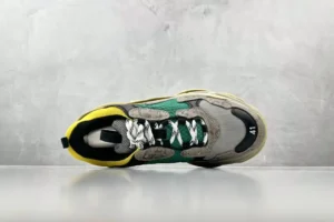 Gucci x Balenciaga Triple S sneaker featuring a multicolored design with gray, green, and yellow accents, showcased against a gray background.