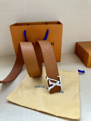 4.0-wide LV Shadow belt with Monogram displayed on a beige pouch and orange shopping bag, featuring the Louis Vuitton logo.