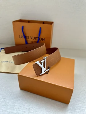 4.0-wide LV Shadow belt with Monogram displayed on a box, featuring a silver LV buckle and an orange Louis Vuitton shopping bag in the background.