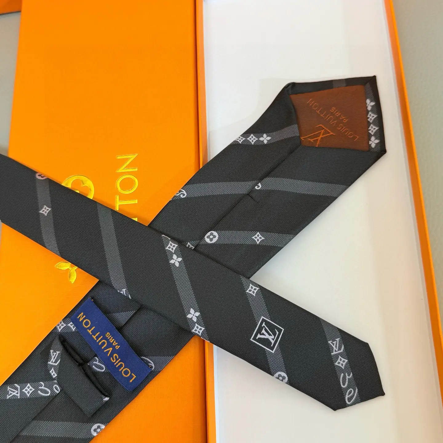 Silk LV tie featuring diagonal stripes, LV logo, and Monogram flowers, displayed in an orange Louis Vuitton box, ideal for both casual and formal wear.