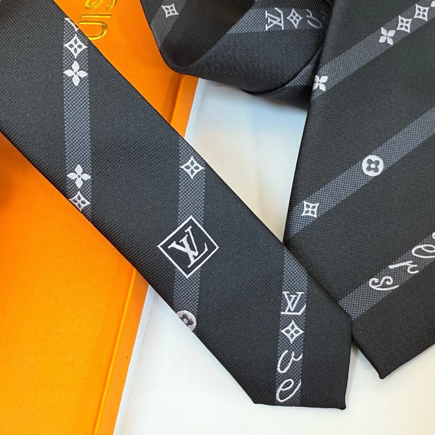 Silk tie featuring LVVers logo and Monogram flowers in diagonal stripe design, displayed on an orange surface, emphasizing luxury and versatility for casual and formal wear.