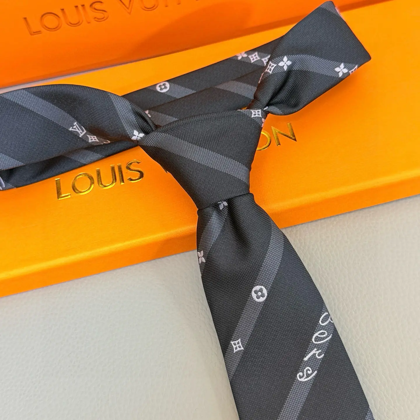Silk LV tie featuring diagonal stripes and LVVers logo, displayed on an orange Louis Vuitton box, emphasizing luxury and elegance for versatile styling.