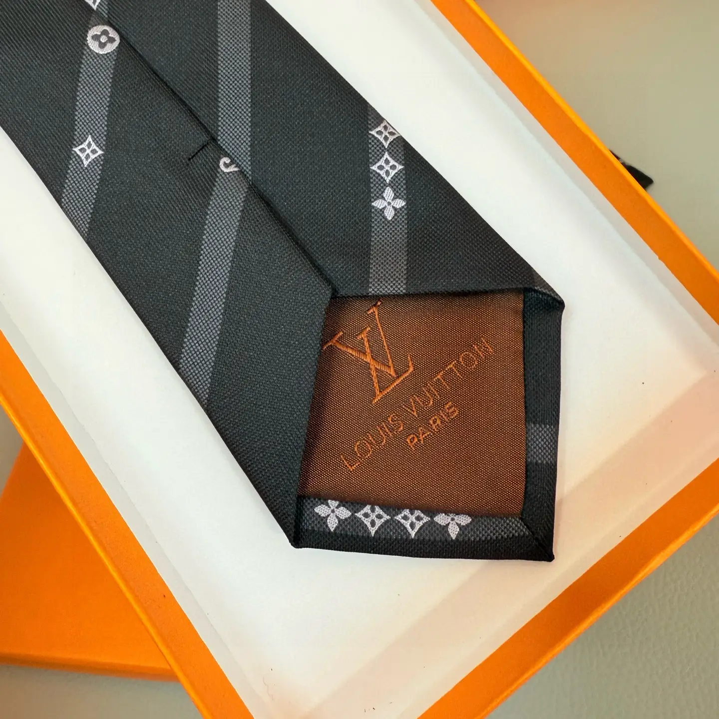 Silk tie featuring LVVers logo and Monogram flowers in diagonal stripe design, placed on a light background with an orange box.