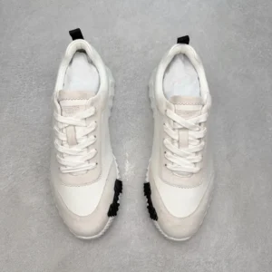 Hermes Men’s Bouncing Sneaker in technical mesh, featuring a white upper with black accents, displayed on a gray surface, emphasizing luxury and craftsmanship in replica footwear.