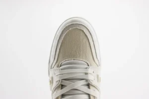 Top view of a Tyler x Louis Vuitton Trainer low cut sneaker featuring a combination of beige and white materials, showcasing intricate stitching and laces, emphasizing luxury craftsmanship.