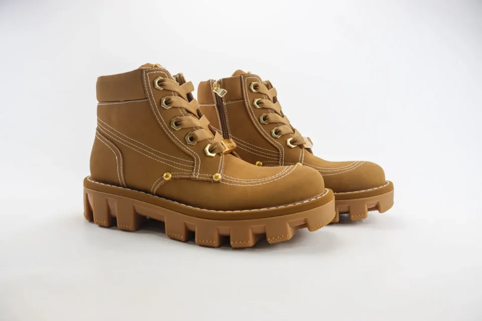 [Brand] boots model with brown colorway tan leather and chunky lugged sole with gold eyelets and zipper
