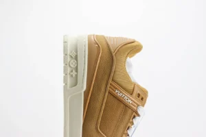 Louis Vuitton Trainer low-cut casual sneaker in tan and white, showcasing textured upper and distinctive logo details, ideal for luxury footwear enthusiasts.