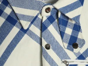 No visible brand or product type; close-up of a blue and white plaid fabric with silver snap buttons and a silver zipper