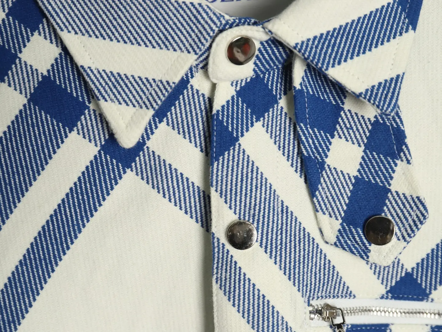 No visible brand or product type; close-up of a blue and white plaid fabric with silver snap buttons and a silver zipper