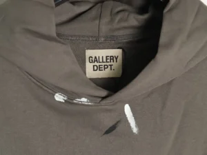 GALLERY DEPT. hoodie featuring a close-up of the label and unique ink splashes on a soft, brown fabric, highlighting the craftsmanship and artistic design of the GD Inkjet Hot Stamped Letter Hoodie.