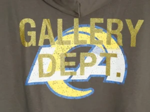 GALLERY DEPT. hoodie featuring bold gold and blue ink-stamped logo design on a brown background, emphasizing craftsmanship and trendy fashion.