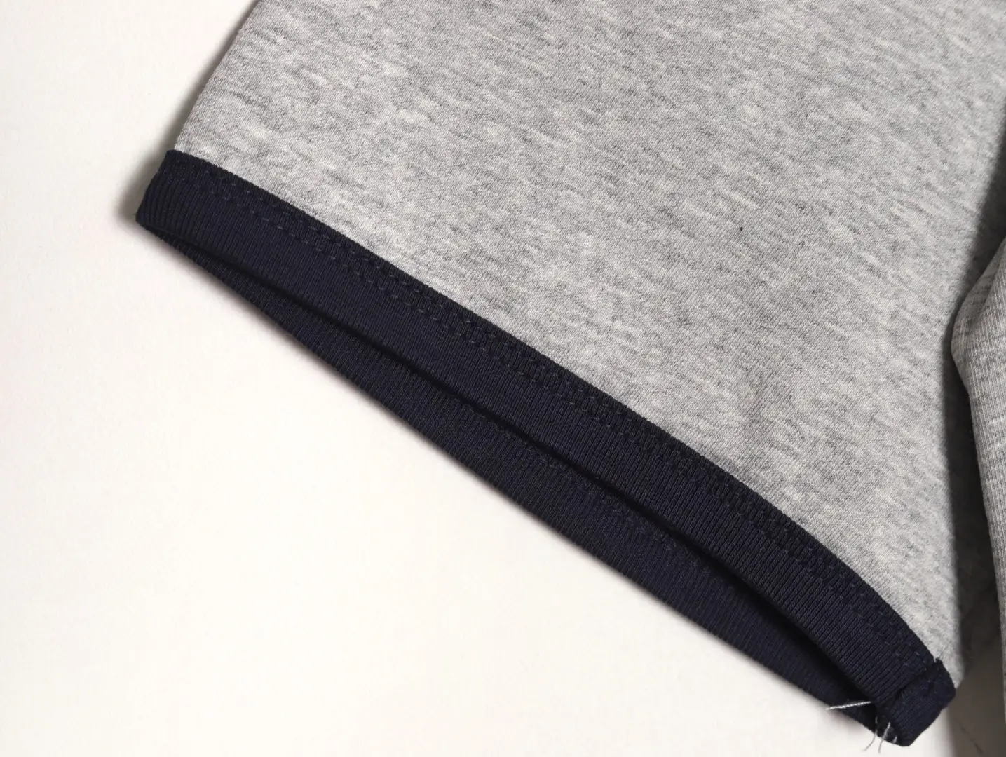 I see the image shows a close-up of a garment sleeve edge with grey fabric and navy blue trim, but no brand or model information is visible. Please provide the product details or another image with the product name, brand, or specific type for accurate alt text according to your SEO rules.
