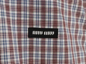 MIU MIU logo on brown and blue fine grid patterned fabric of a long sleeve shirt, showcasing luxury fashion craftsmanship.
