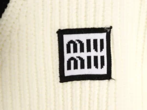 Miu Miu logo patch on a cream-colored cardigan, emphasizing luxury fashion branding and design details.