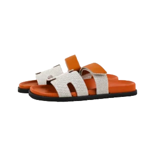 Hermes slippers featuring a stylish design with orange accents and a woven texture, showcased as part of a luxury footwear collection available for purchase.