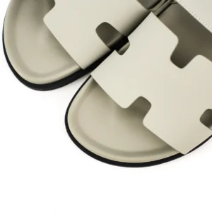 Hermes flat one-word slippers in beige, featuring a distinctive cut-out design, showcasing the luxury footwear's sleek profile and high-quality material.