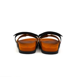 Hermes slippers featuring a flat bottom design with black straps and an orange sole, showcasing luxury footwear style and quality materials.