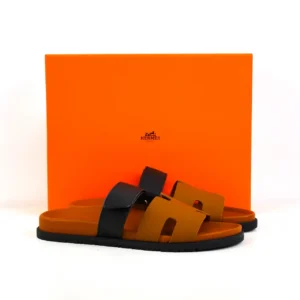 Hermes slippers in brown and black, displayed in front of an orange box with the Hermes logo, highlighting luxury footwear options available for pre-sale.