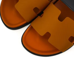 Hermes slippers featuring a flat design with an iconic logo in orange and black, showcasing luxury footwear style and comfort.