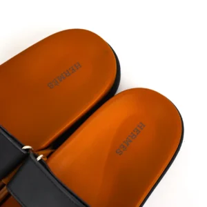 Hermes slippers featuring a sleek black strap and distinctive orange footbed with embossed "Hermes" logo, showcasing luxury footwear design.