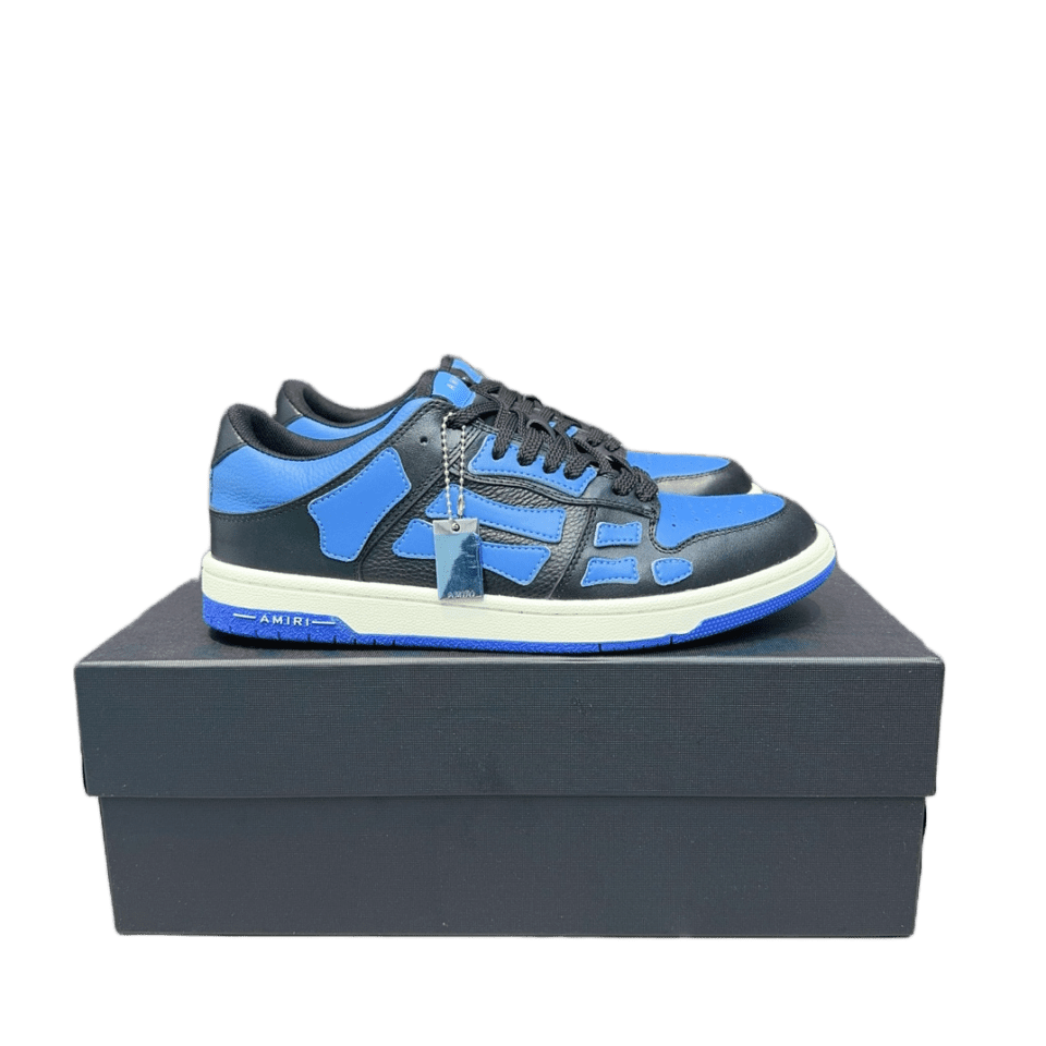 Black and blue AMIRI Trainer sneakers displayed on a black shoe box, featuring a modern design and a price tag.