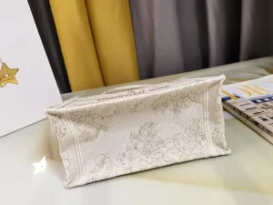 Dior Small Gold Dream Rêve d’Infini Pattern Tote displayed on a table, featuring intricate embroidery and the CHRISTIAN DIOR Paris logo, showcasing luxury craftsmanship.