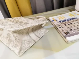 Dior Small Gold Dream Rêve d’Infini Pattern Tote on a table beside a magazine, showcasing elegant design and craftsmanship.