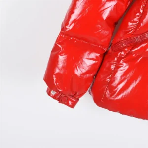 Red Moncler jacket sleeve featuring shiny fabric, zip detail, and elastic cuff, emphasizing slim fit design.