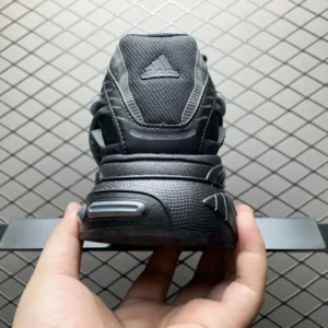 Black Pharrell x AD Adistar Jellyfis shoes featuring a prominent Adidas logo on the heel, showcasing a sleek design with a textured finish and futuristic aesthetic, held in a hand against a geometric background.