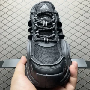 Pharrell x AD Adistar Jellyfis shoes in black, showcasing a futuristic design with three stripes, textured materials, and a prominent TPU sole, held in hand against a textured background.