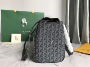 Goyard Rouette bag in gray fabric with distinctive pattern, featuring a white strap and set against a green Goyard shopping bag and accessories on a marble surface.