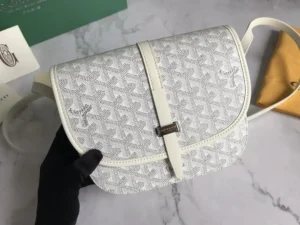 Goyard Belv é d è re Single Mailman Bag in white with signature pattern, featuring a narrow buckle and adjustable shoulder strap, displayed on a marble surface.