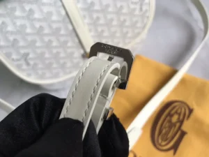 Close-up of Goyard Belv é d è re Single Mailman Bag strap with metal buckle detail, showcasing premium leather and craftsmanship against a soft background.